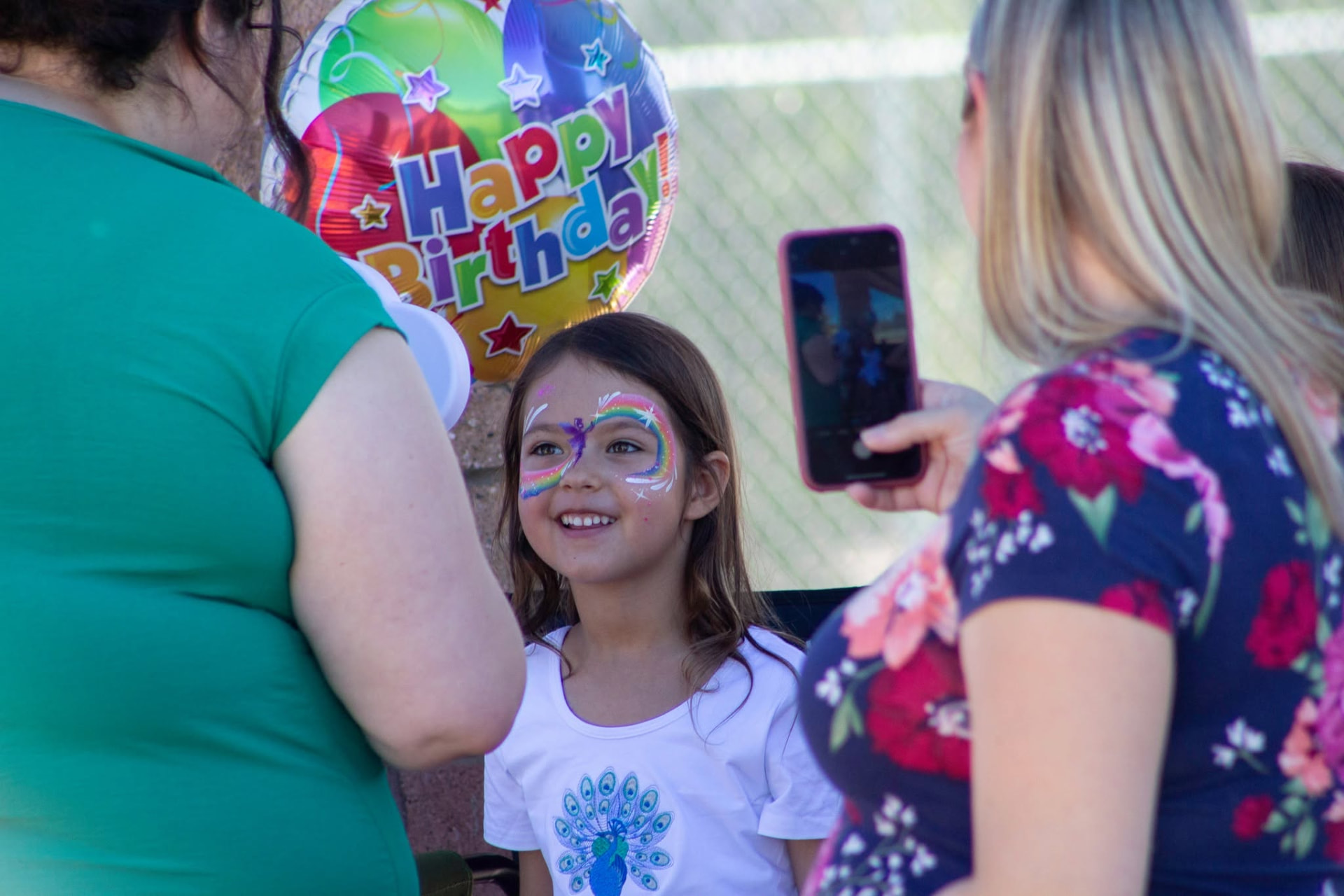 A smiling child showing off rainbow fairy face paint at a Tucson birthday party